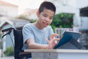 Ungur drengur í hjólastól situr við borð með ipad fyrir framan sig sem hann er að nota.