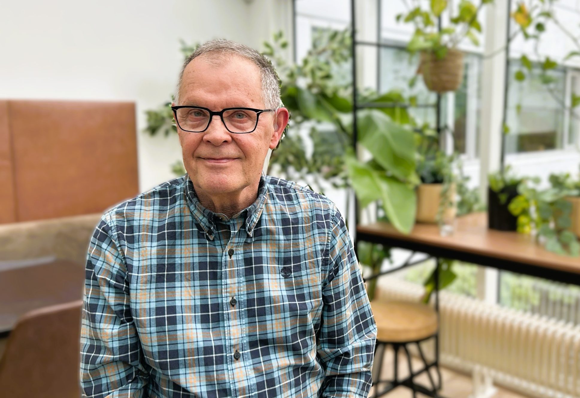 Uppstillt mynd af Ingólfi þar sem hann situr í glerskála með plöntur í bakgrunni.